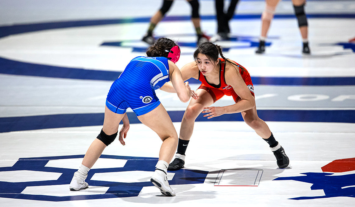 Two wrestlers in blue and red uniforms competing on a Dollamur wrestling mat at the USA Wrestling US Open