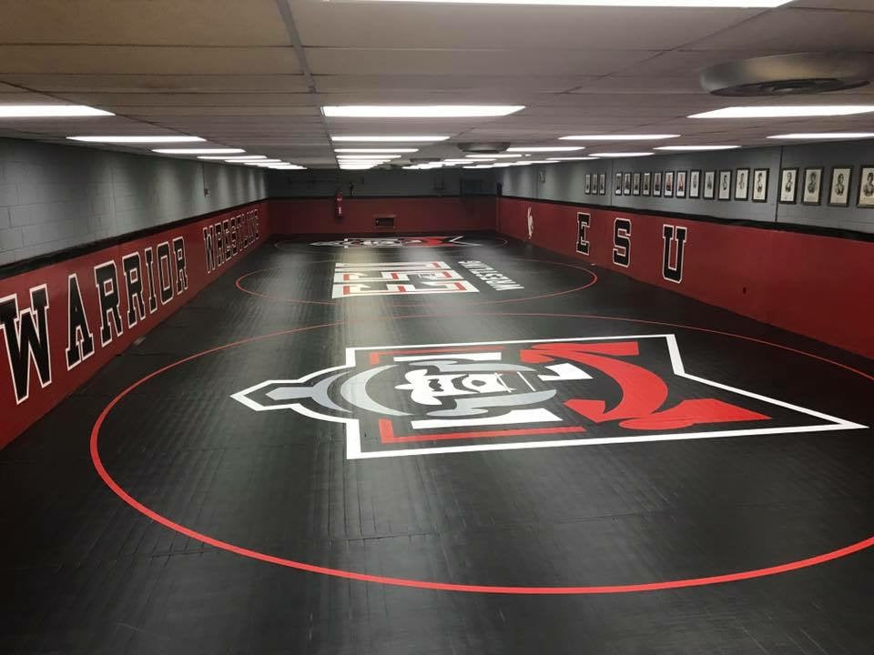 Black, red, and grey wrestling room with the ESU logo, text, and 'Warrior' branding