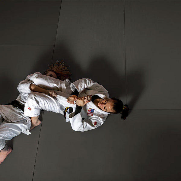 Women in white martial arts gis grappling on a floor made of grey Swain Mats by dollamur