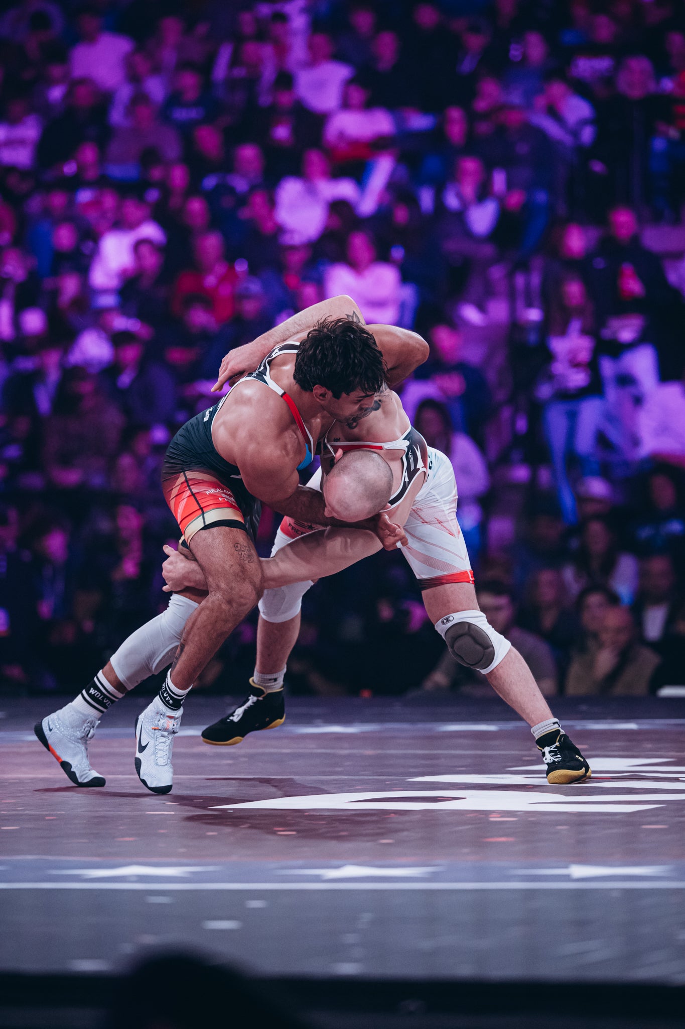 Two wrestlers competing on a Dollamur wrestling mat with a crowd in the background