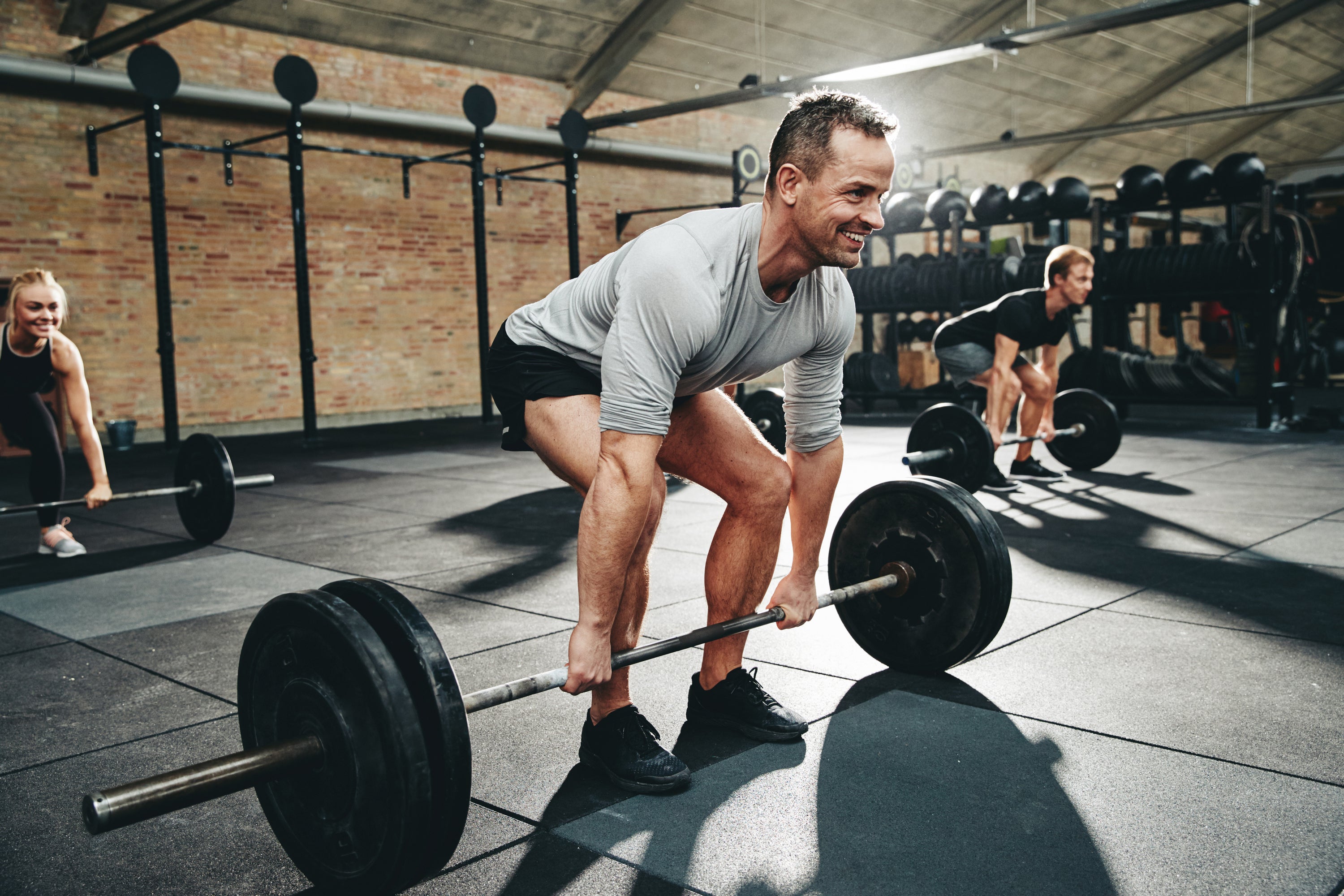 Man lifting a barbell in a gym setting with other people in the background and Dollamur gym flooring made of high-performance rubber
