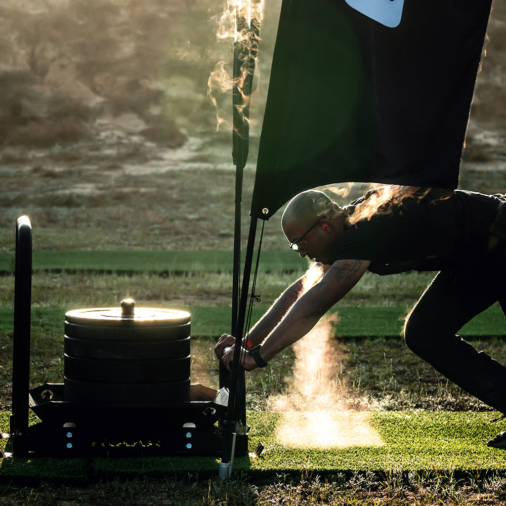 a Tactical Games athlete breathing steam while pushing a weighted sled on GymTurf on a cold morning